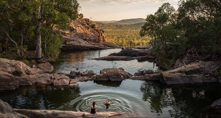 Lumière dorée sur un bassin de gorge isolé où deux nageurs créent des ondulations au milieu de formations rocheuses spectaculaires