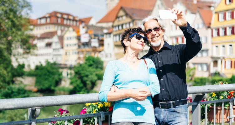 Ein Paar, das ein Selfie auf einer Brücke mit bunten Gebäuden im Hintergrund macht.