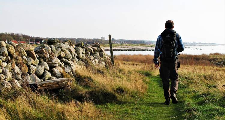 Person walking along a shoreline path next to stone wall.