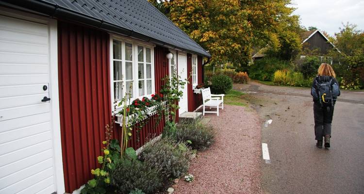Person walking past red wooden houses on a street.