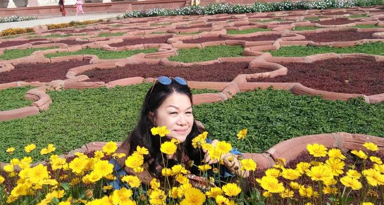Frau, die durch gelbe Blumen späht, mit Gärten im Hintergrund.