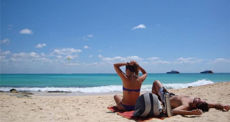 Couple se prélassant sur une plage de sable des Caraïbes avec une eau turquoise et des navires de croisière à l'horizon