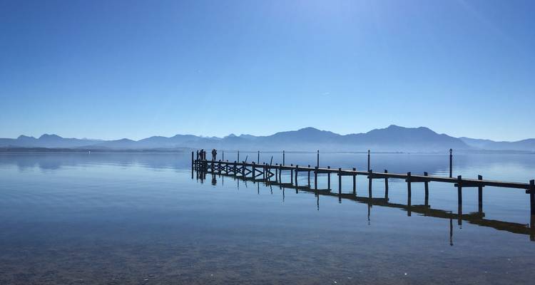 Lange houten pier strekt zich uit over het spiegelgladde meer richting het wazige bergsilhouet