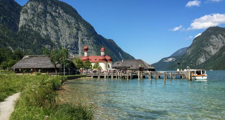 De uivormige koepelkerk St. Bartholomä staat op een houten pier naast het heldere turquoise water van de Königssee, omlijst door steile alpine kliffen.