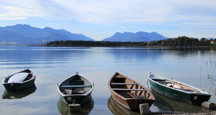 Ruderboote an einem ruhigen See mit einer Bergkette in der Ferne.
