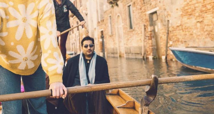 Ein Gondolier rudert entlang eines engen Venezianischen Kanals, während die Passagiere die Fahrt geniessen.