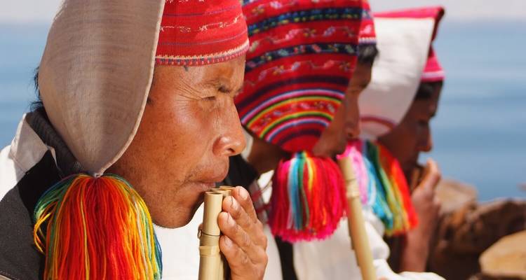 Drei Personen in traditioneller Kleidung spielen Bambusflöten.