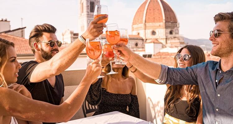 Groupe d'amis trinquant avec des Aperol Spritz sur un toit avec le dôme du Duomo de Florence en arrière-plan.