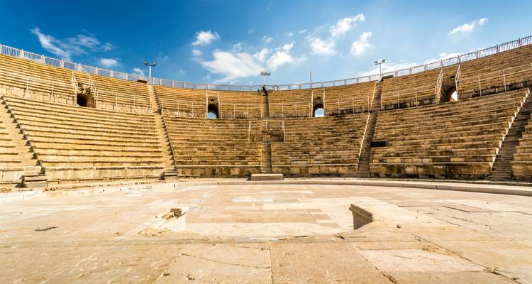 Amphithéâtre de style romain antique avec des gradins en pierre sous un ciel lumineux.