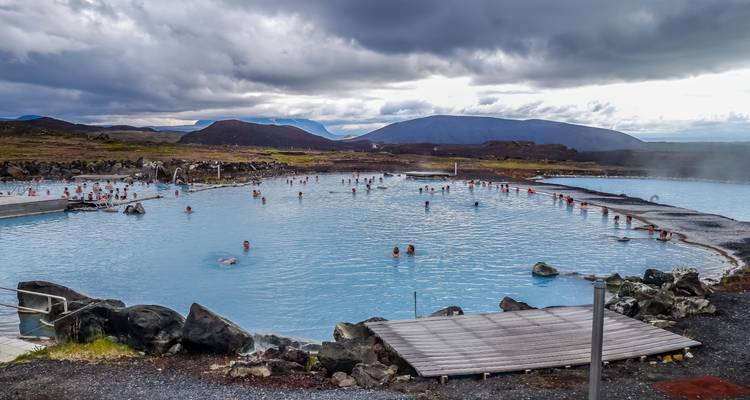Geothermal spa with people relaxing in hot blue waters amid a rocky landscape.