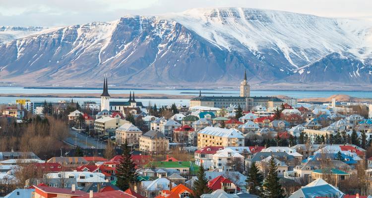 Colorful cityscape against snow-covered mountains with clear skies.