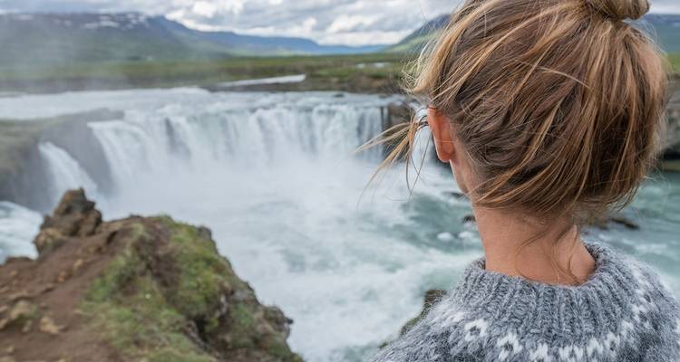 Person observing a powerful waterfall with rocky landscape.