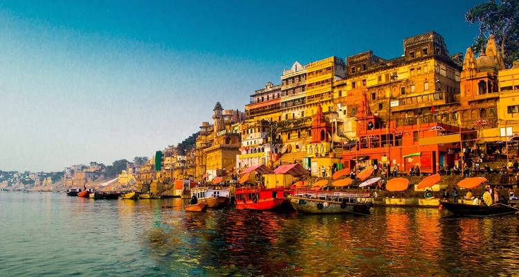 Colorful ghats along a river with boats in Varanasi at sunrise.