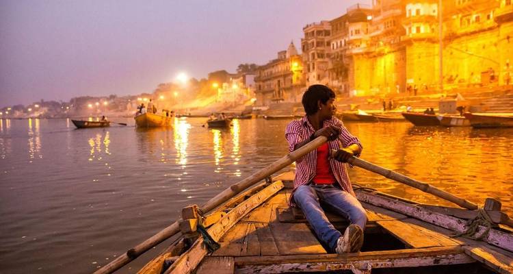 A man rowing a boat on the Ganges river in Varanasi during twilight.