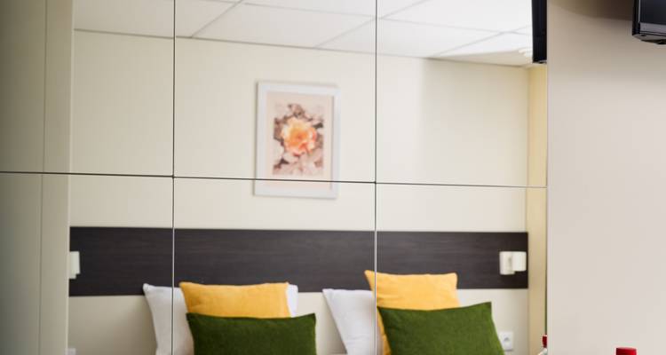 Reflet d'une chambre d'hôtel avec des oreillers verts et jaunes contre une tête de lit.