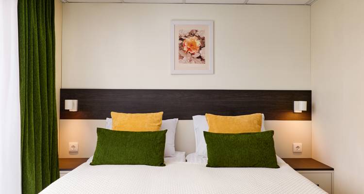 Plan rapproché d'un lit d'hôtel avec des oreillers verts et jaunes contre une tête de lit sombre.