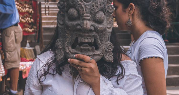 Een persoon die een traditioneel masker vasthoudt tussen een drukke marktomgeving.