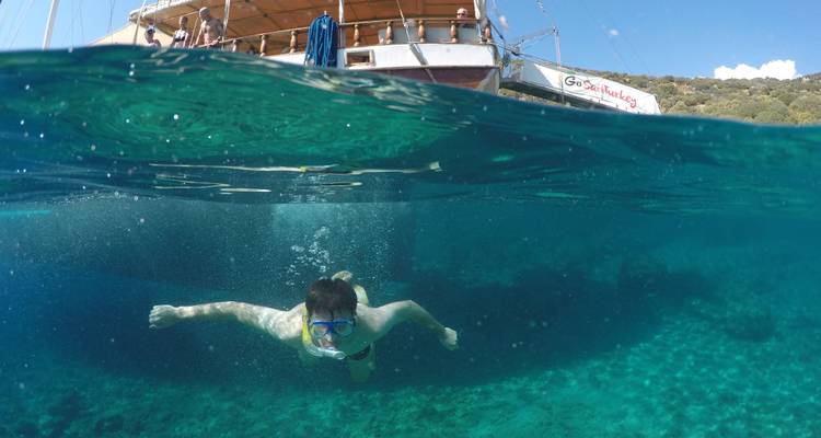 Person snorkeling beneath a boat in clear blue water.
