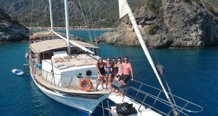 Group of people on a sailboat with rocky coastline.