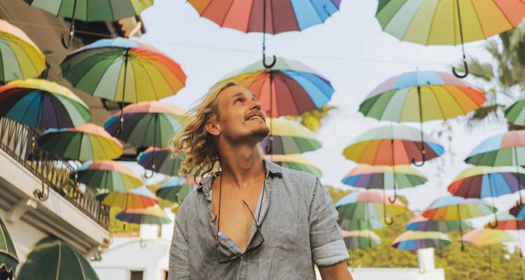 Person looking up at colorful umbrellas hanging overhead.