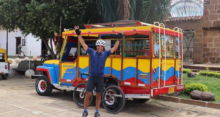 Cycliste prenant la pose devant un véhicule coloré avec une église en arrière-plan.