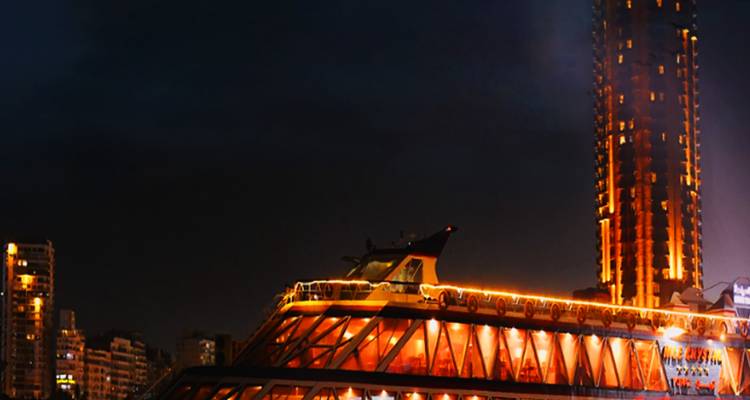 Paysage urbain nocturne avec des bâtiments illuminés et un bateau de croisière.