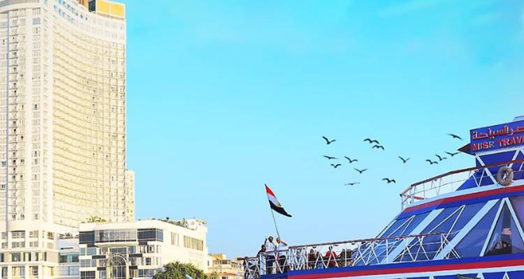 Un grand bâtiment et un navire de croisière avec un drapeau et des oiseaux dans un ciel bleu clair.