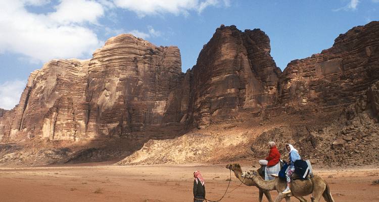 Des gens chevauchant des chameaux à travers un désert dans le Wadi Rum.