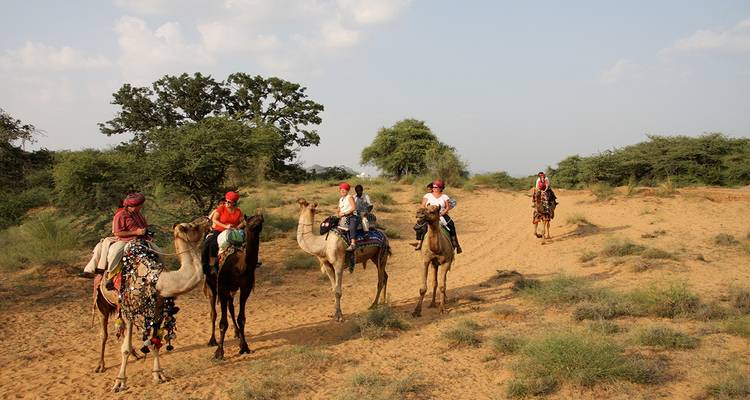 Gruppe von Menschen, die auf Kamelen in einer Wüstenlandschaft reiten.