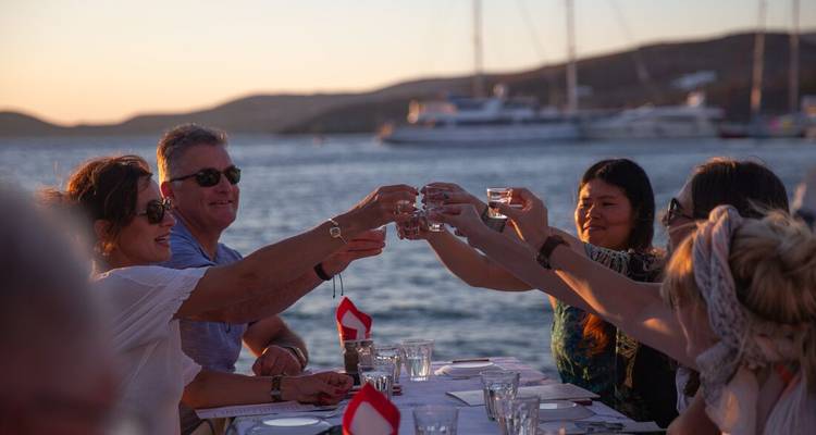 Los amigos alzan las copas en un brindis junto al mar mientras los yates descansan de fondo al atardecer