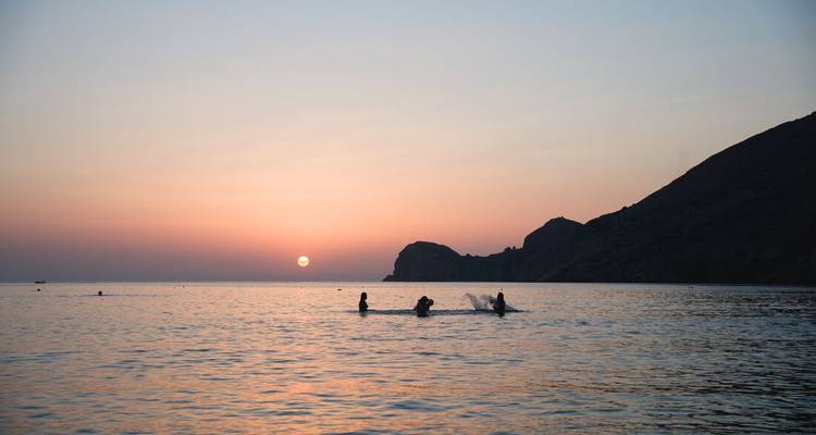Gente en silueta pescando desde un bote pequeño contra un atardecer en tonos pastel