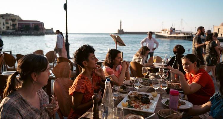 Restaurante al aire libre concurrido junto a un puerto con comensales disfrutando de comida y bebidas