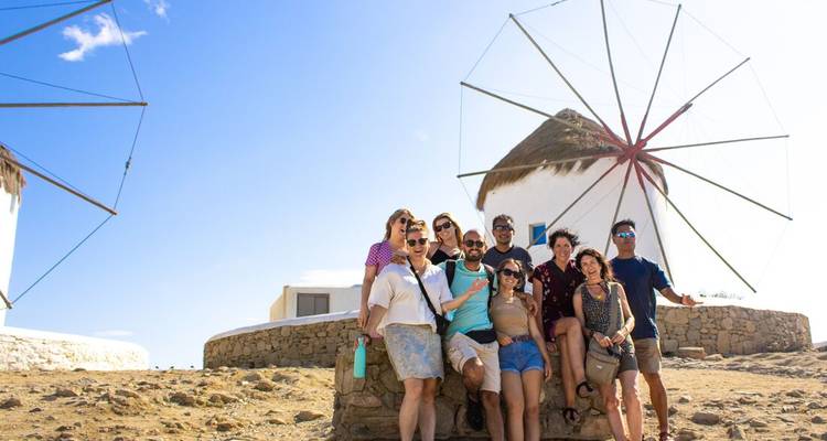 Grupo de turistas sonriendo posando junto a los icónicos molinos de viento de Mykonos en un día soleado