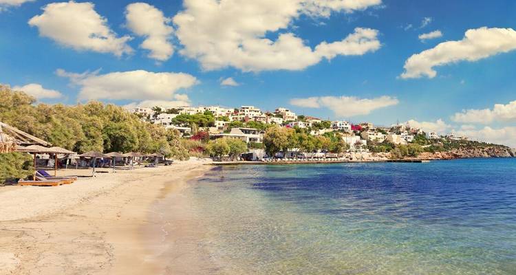 Playa tranquila y arenosa con tumbonas y un pueblo costero bajo nubes esponjosas