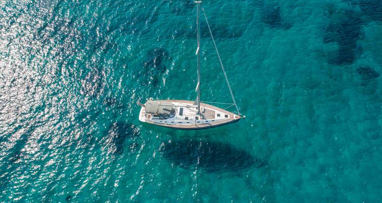 Un velero solitario flota sobre agua turquesa cristalina vista desde arriba