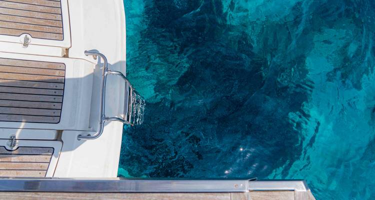 Primer plano de la plataforma de baño del yate con escalera descendiendo hacia el agua azul profundo