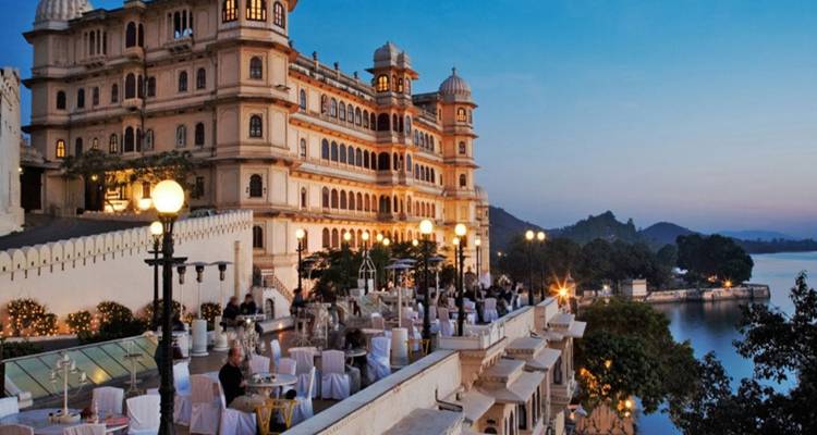 Un balcón de palacio preparado para una cena con vistas panorámicas de un lago y colinas al atardecer.