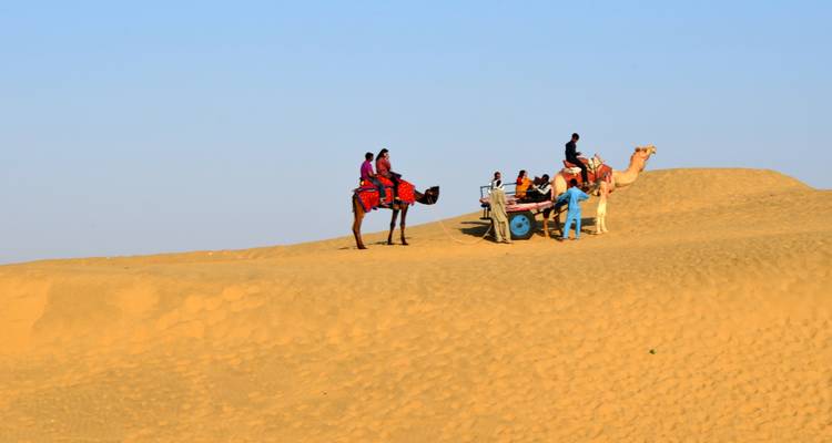 Personas montando camellos a través de un paisaje desértico en la luz del atardecer.