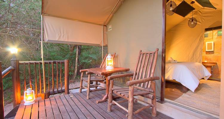 Holzterrasse mit Stühlen und Laternen vor einem Zelt.