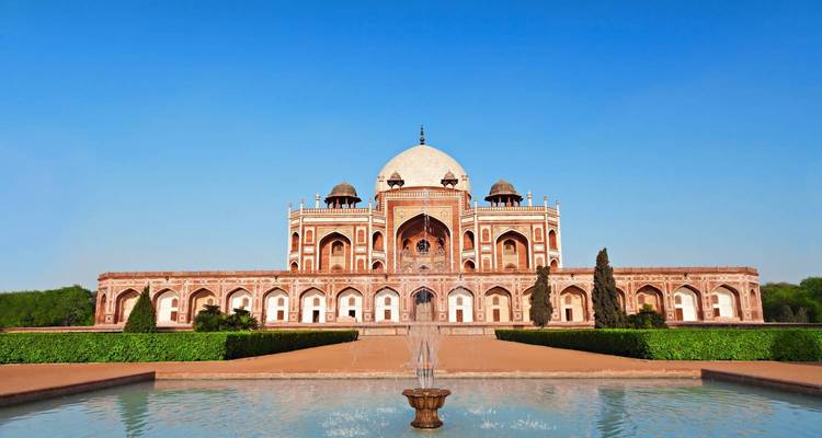 Mausoleum surrounded by manicured gardens and a reflection pool under a clear blue sky.