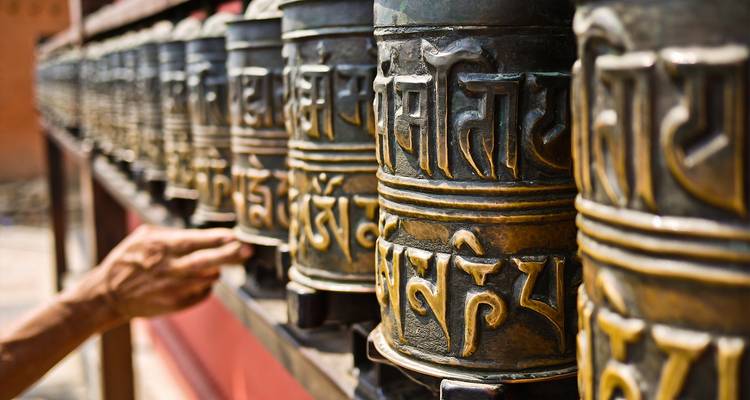 Een persoon die gebedsmolens met inscripties draait in een tempel.