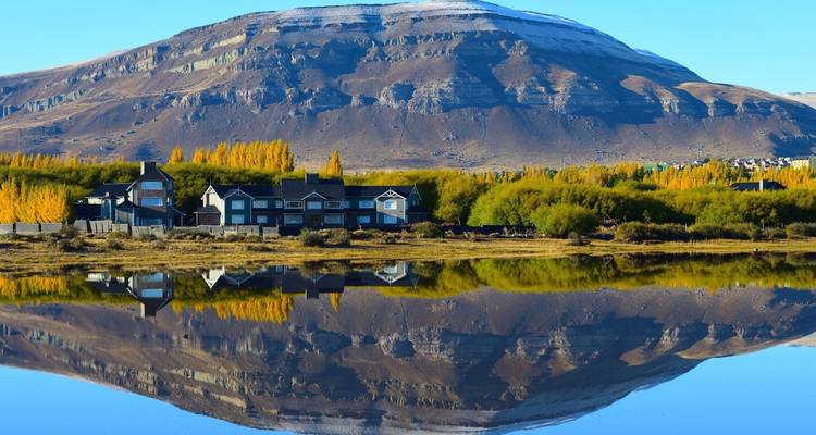 Häuser, die sich in einem ruhigen See mit Bergkulisse spiegeln.
