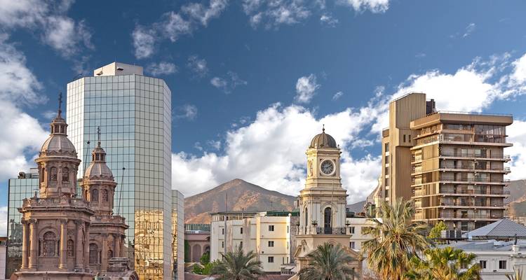 Un paisaje urbano con edificios modernos e históricos sobre un fondo de montañas.