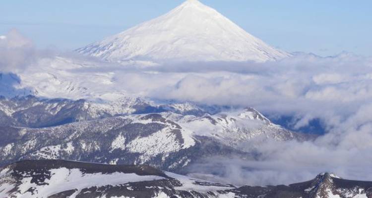 Picos montañosos cubiertos de nieve parcialmente oscurecidos por nubes.