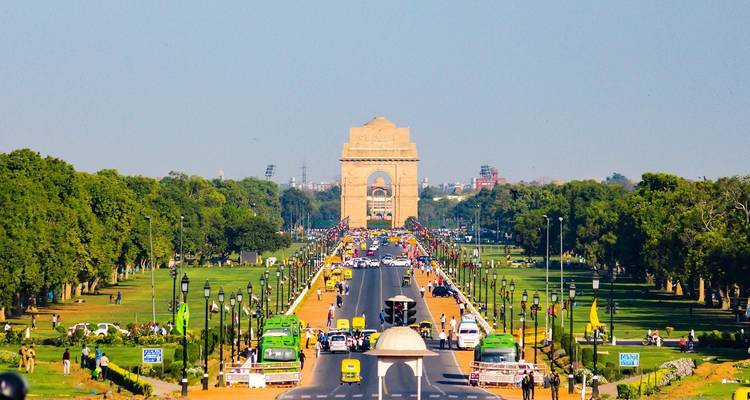 Zicht op India Gate van een afstand omringd door weelderig groen en verkeer.