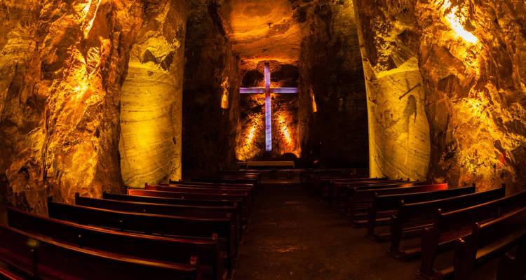Zoutkathedraal met verlicht kruis en kerkbanken binnen grottachtige muren.