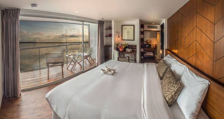 Luxuriöse Flusskreuzfahrt-Kabine mit Kingsize-Bett, Balkonbestuhlung und panoramischen Wasserblicken im warmen Abendlicht.