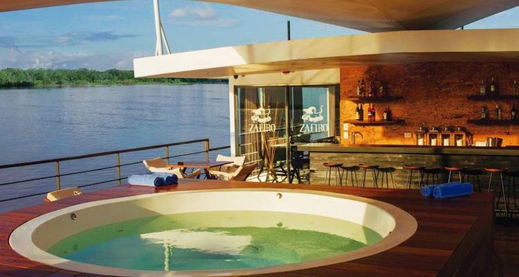 Offenes Deck mit rundem Whirlpool, Barbereich und Flusskulisse unter klarem Himmel.