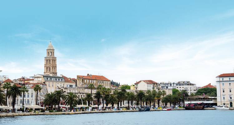 La promenade en bord de mer de Split, bordée de palmiers et de cafés, dominée par le clocher sous un ciel bleu éclatant.