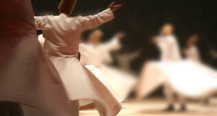 Toma artística difuminada de danzantes derviches giratorios en túnicas blancas rotando durante una ceremonia sufí en un salón tenuemente iluminado.
